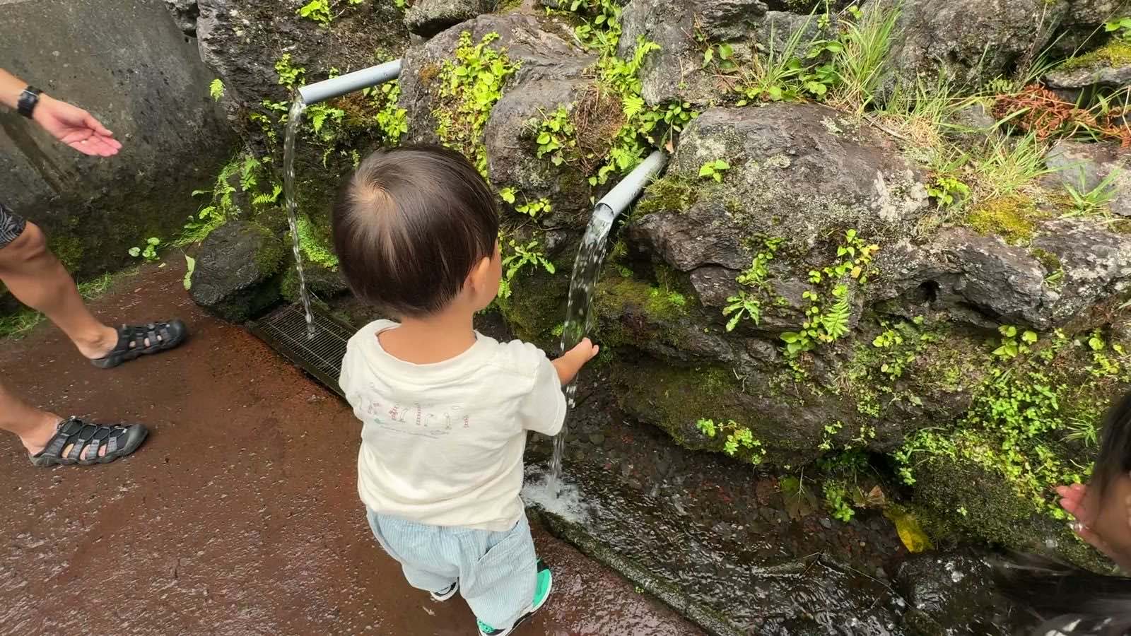 パイプから流れる湧き水にさわる息子