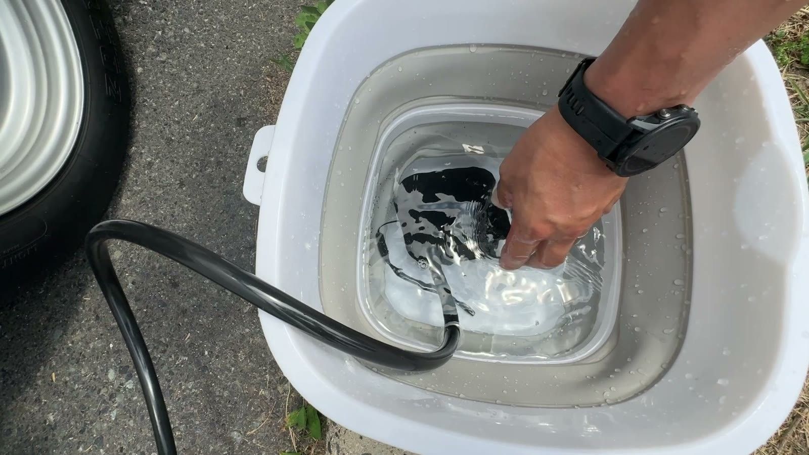 折りたたみバケツの水にポータブルシャワーのポンプを沈める様子