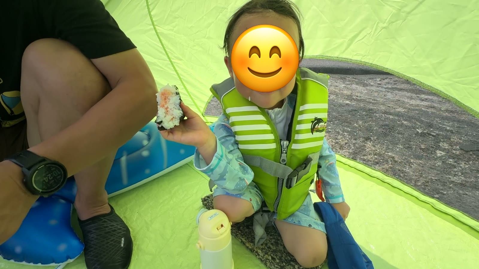 日よけテントの中でおにぎりを持つ3歳の息子
