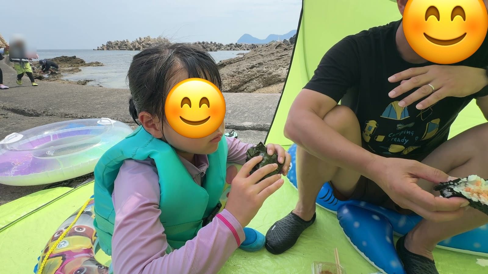 日よけテントでおにぎりを食べる娘とパパ