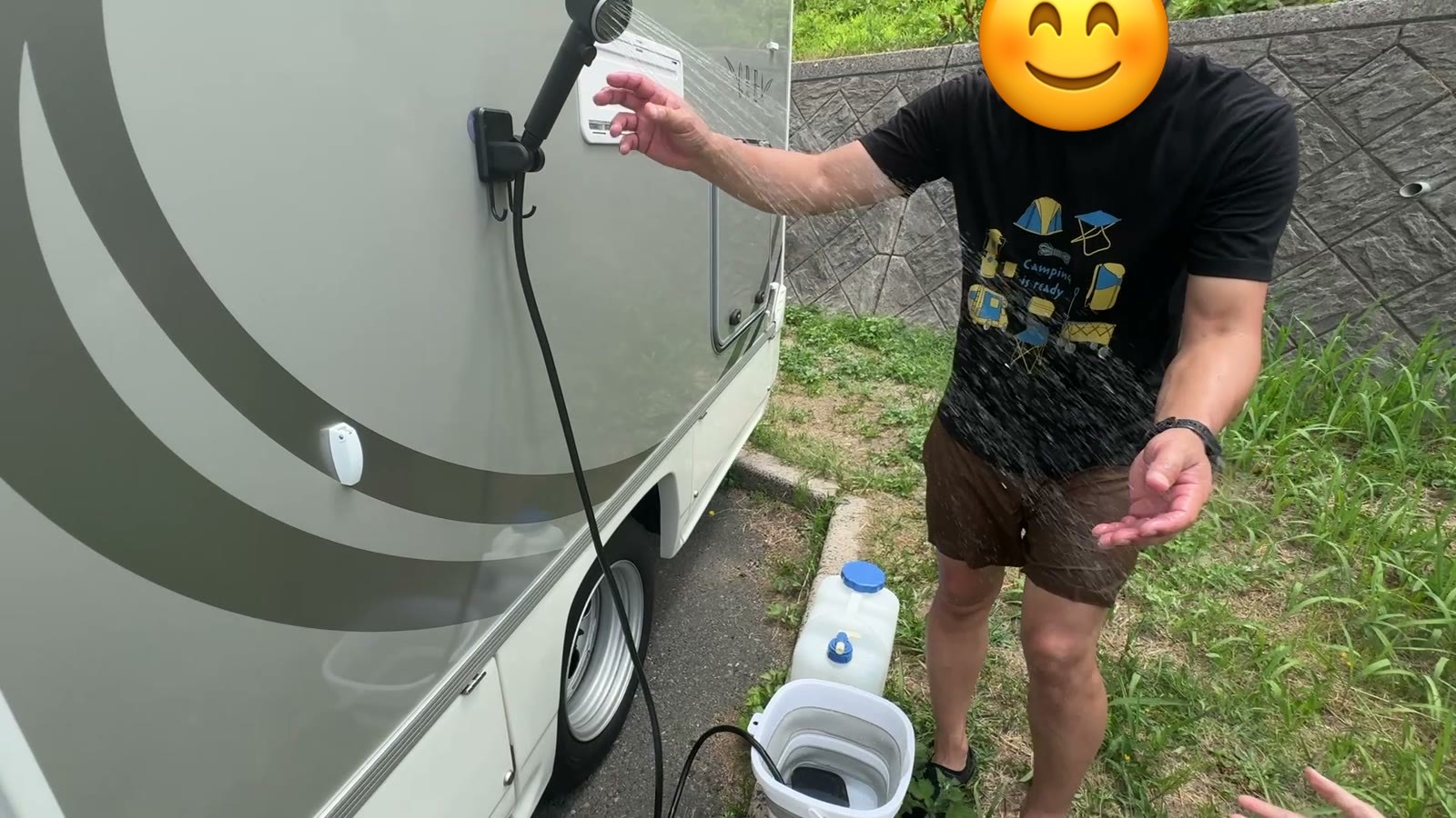 キャンピングカーの横でシャワーの水を確かめるパパ